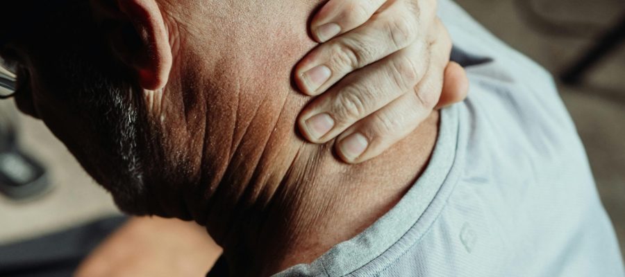 A close-up, high-angle view of an older man's neck as he grips it with his hand, showing signs of stiffness or pain